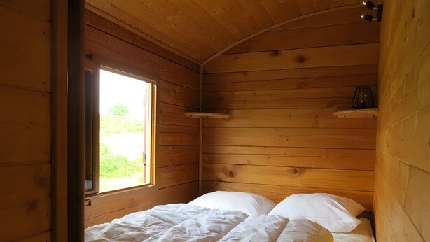Ein Zimmer aus Holz mit einem Bett, einem Fenster und einem Regal.