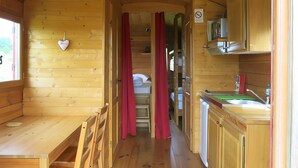 Ein Holzblockbau-Innenraum mit Küche, Essbereich und Schlafzimmer mit Bett und Vorhängen.
