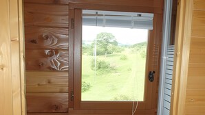 Eine Holzhütte mit kleinem Badezimmer, einem Fenster mit Blick ins Grüne und einem weißen Heizgerät.