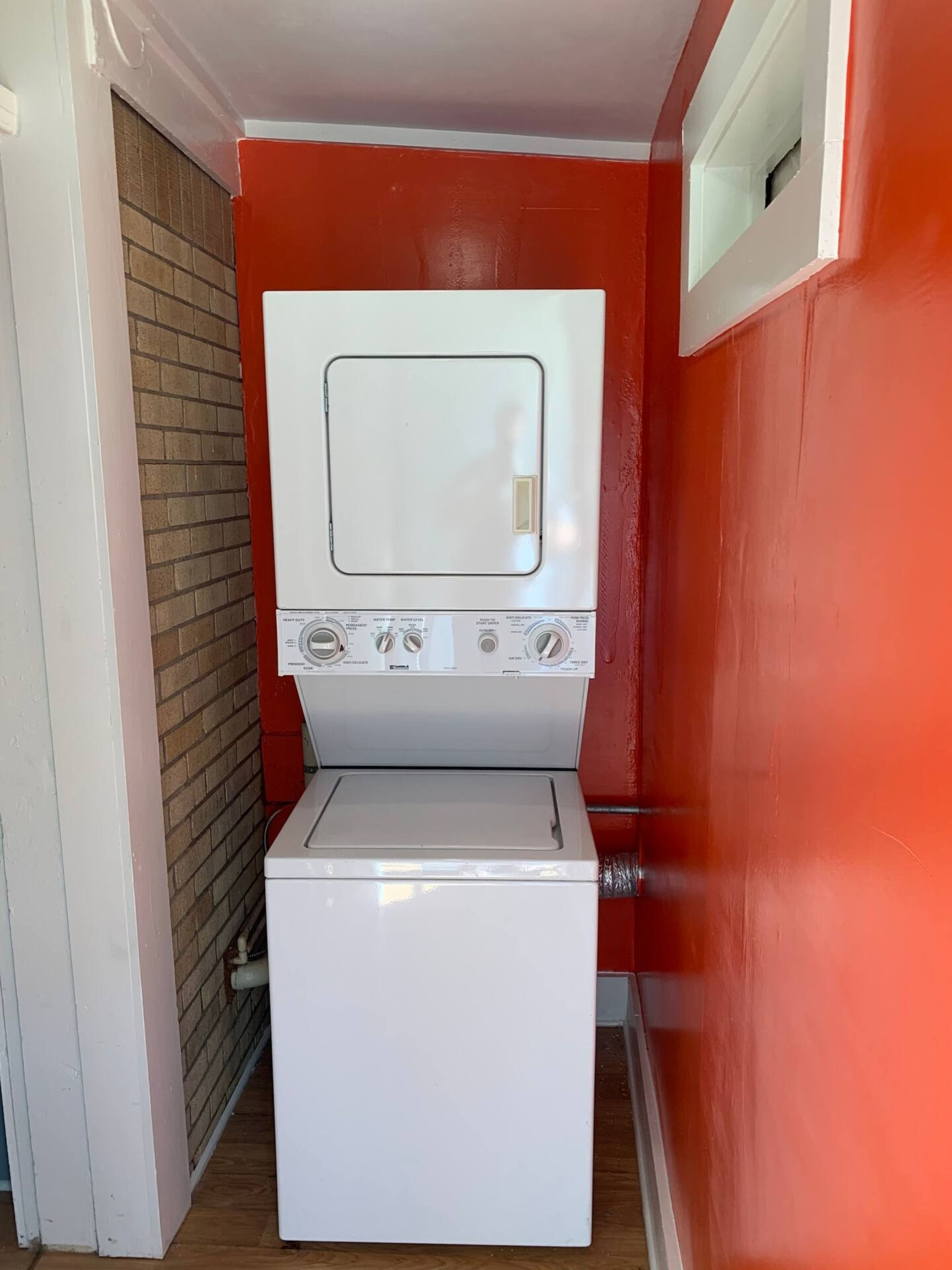 Une petite buanderie blanche avec un mur rouge et une petite fenêtre.