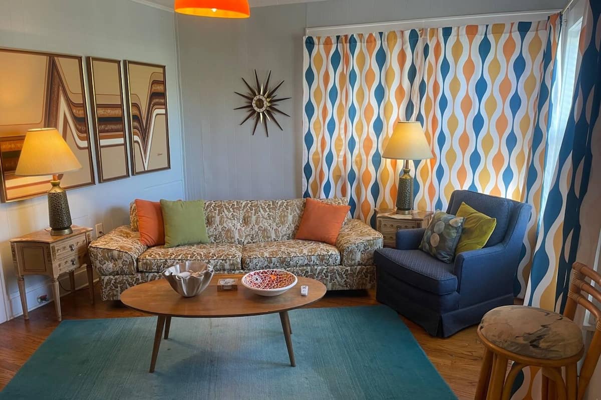 A living room with a patterned sofa, a blue armchair, a round coffee table, and two lamps.
