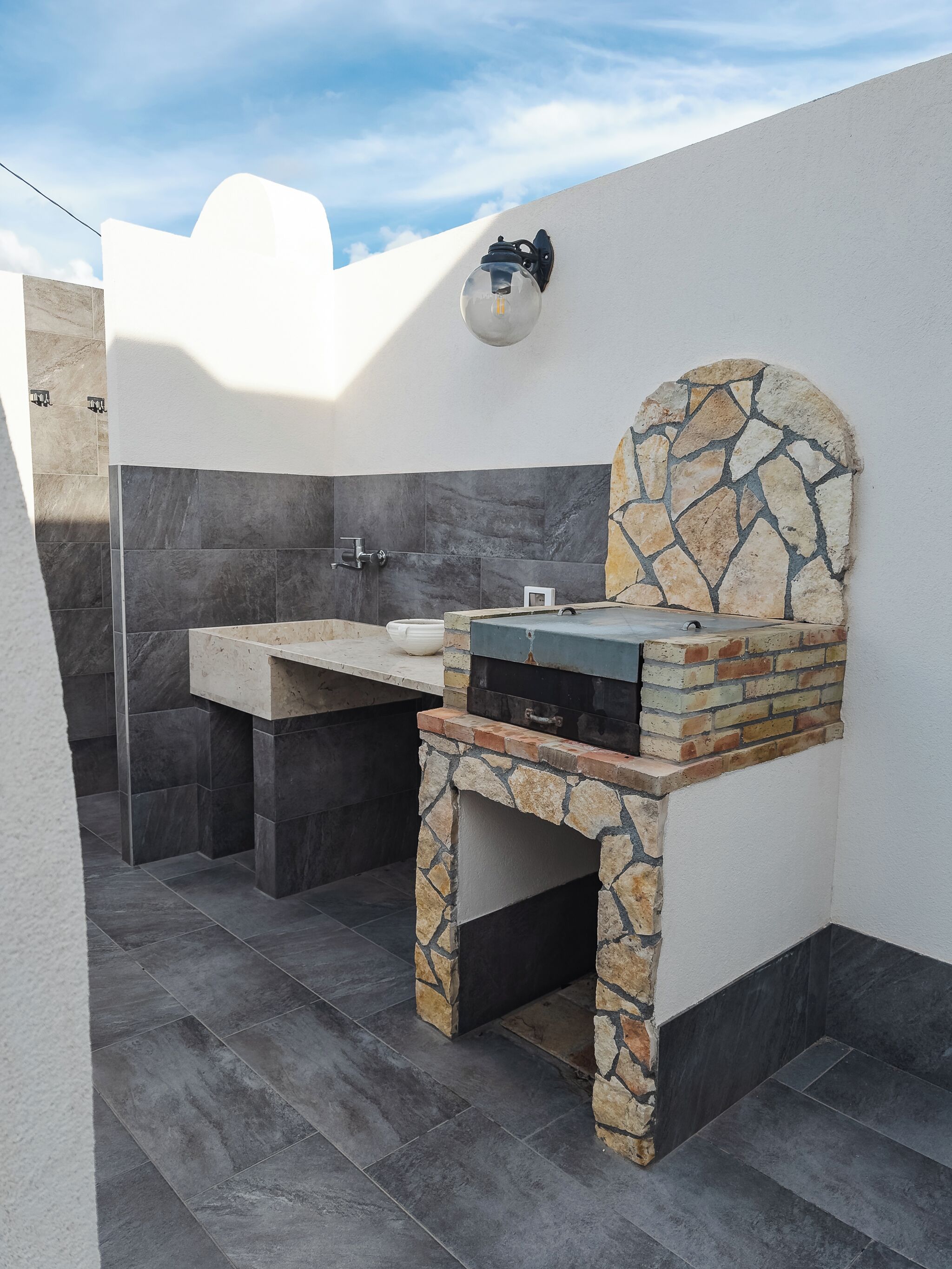 Een badkamer met een stenen wastafel, een douche en een ingebouwde grill.