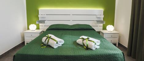 Una cama bien hecha con ropa de cama verde, cabecera blanca y dos mesitas de noche con lámparas.