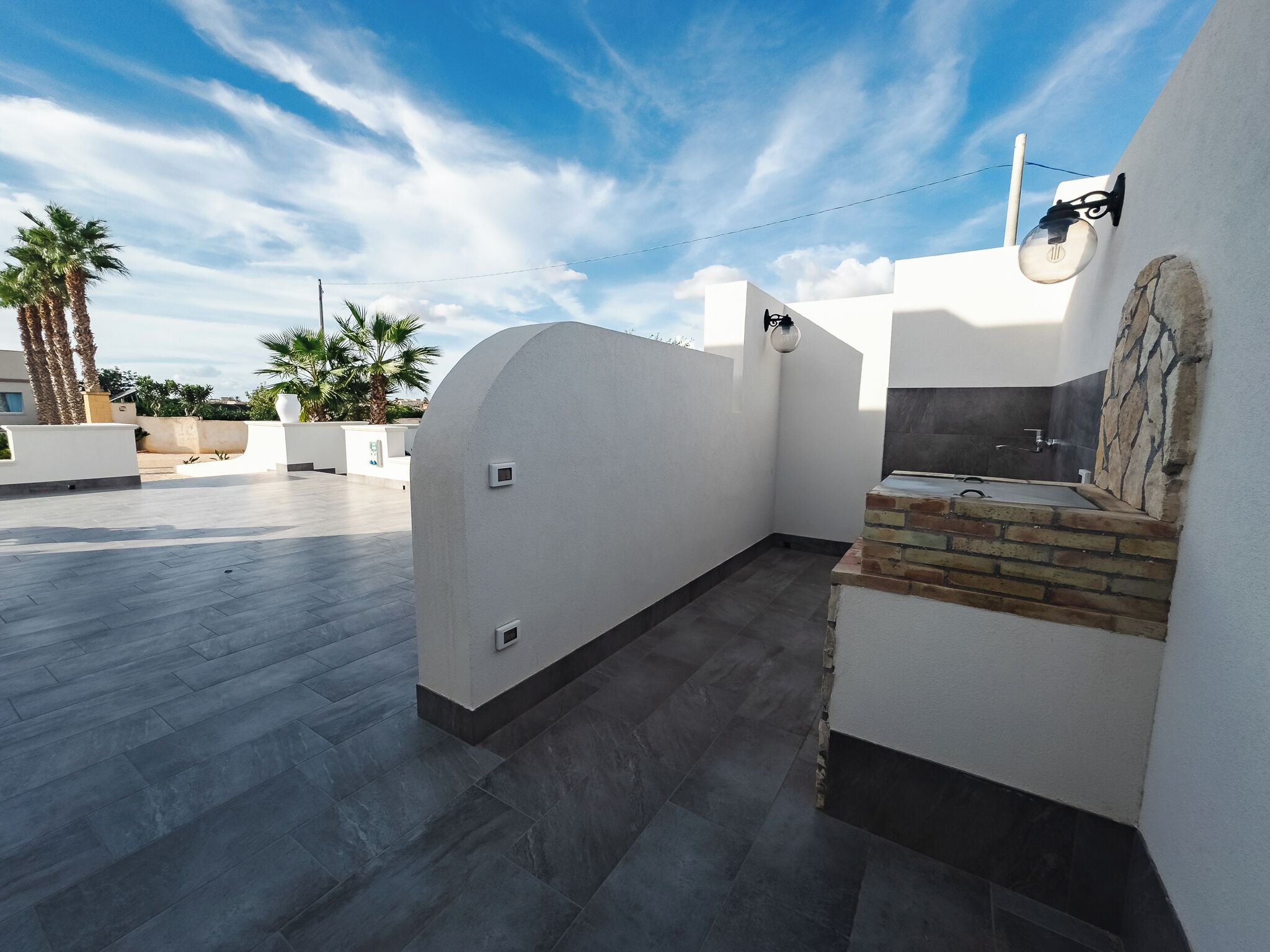 A modern outdoor patio area with a flat roof, a small brick fireplace, and a white wall with a stone accent.