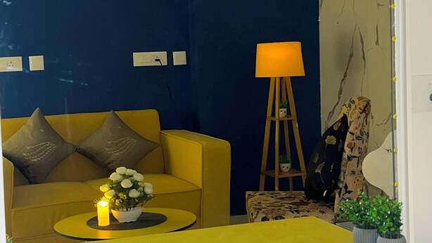 Ein Zimmer mit einem gelben Sofa, einem kleinen runden Tisch mit Kerze, einer Lampe und einem Spiegel.
