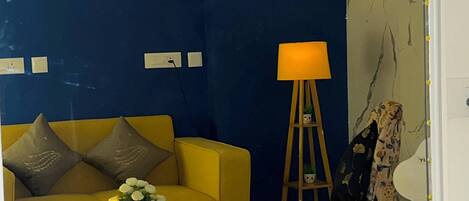 A room with a yellow sofa, a small round table with a candle, a lamp, and a mirror.