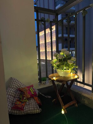 Ein Balkon mit einem Blumentopf, einem karierten Kissen und Snacks.