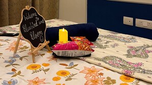 Ein Zimmer mit einem Bett, einem an der Wand befestigten Fernseher, einem Willkommensschild und einer Kerze auf dem Bett.