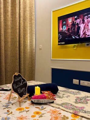 Ein Zimmer mit einem Bett, einem an der Wand befestigten Fernseher, einem Willkommensschild und einer Kerze auf dem Bett.