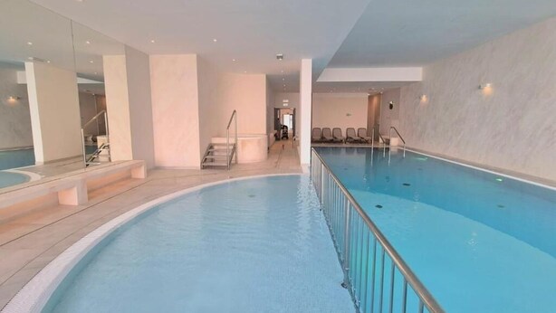 An indoor swimming pool with a clear view of the pool area, a staircase leading to another level, and a seating area with chairs.