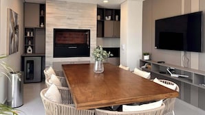 Un salon moderne avec une table à manger en bois, des chaises en osier, un téléviseur à écran plat, des placards intégrés et une cheminée.