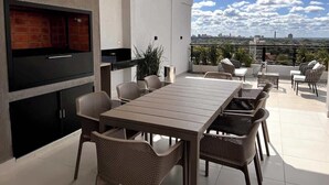Un espace extérieur moderne aménagé pour les repas, avec un téléviseur, un barbecue et des sièges.