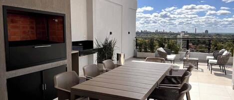 A modern outdoor dining area with a TV, grill, and seating.