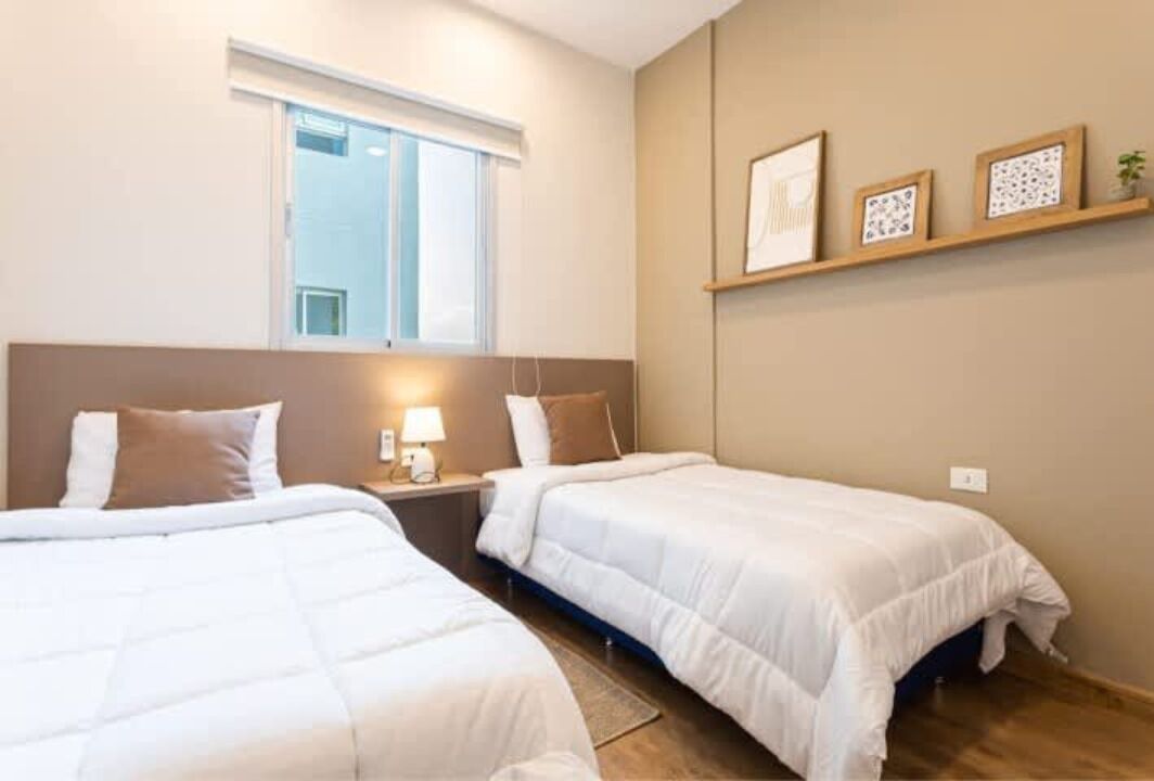 Et hotelværelse med to senge, et vindue, et natbord med lampe og billeder hængende på væggen.