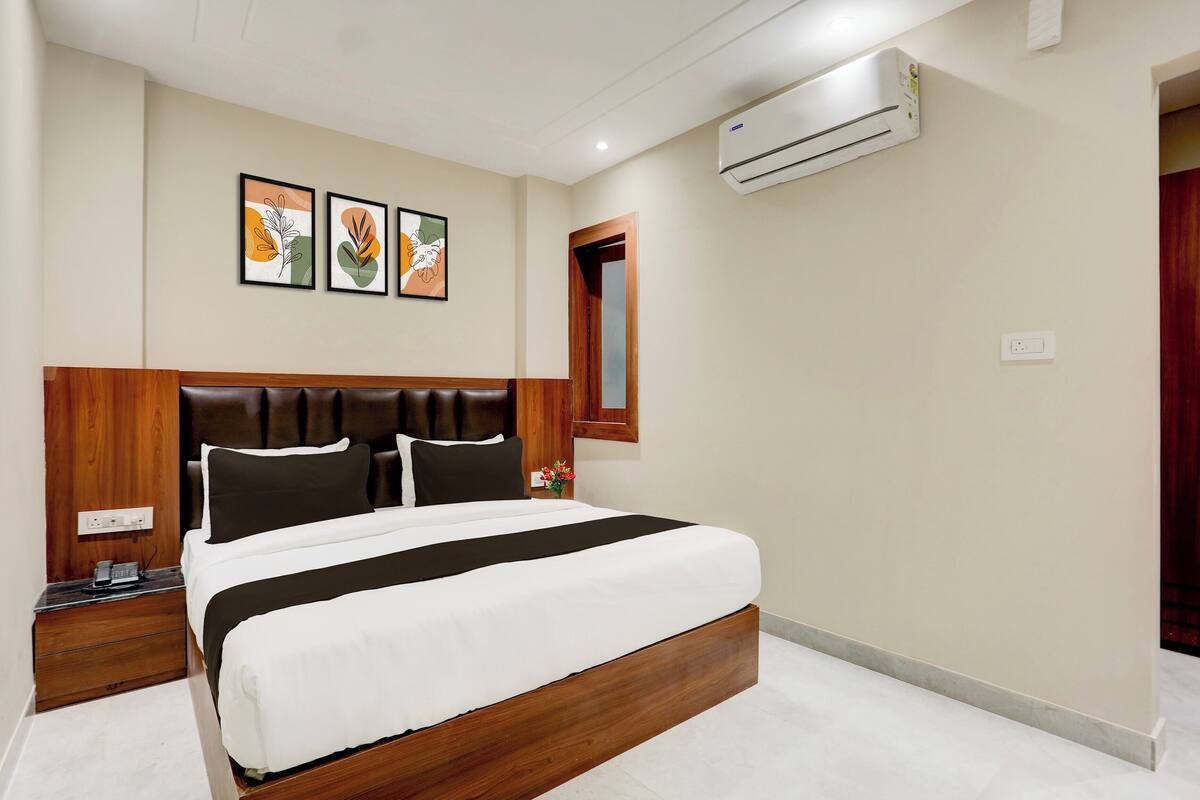 Habitación de hotel con una cama grande, cabecera de madera, mesitas de noche, aire acondicionado y cuadros en la pared.