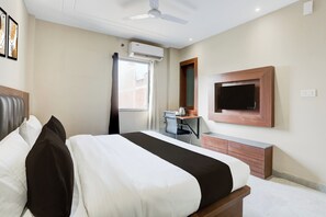 Hotellihuone, jossa on sänky, työpöytä, tuoli, ilmastointilaite, televisio ja ikkuna, jossa on verhot.