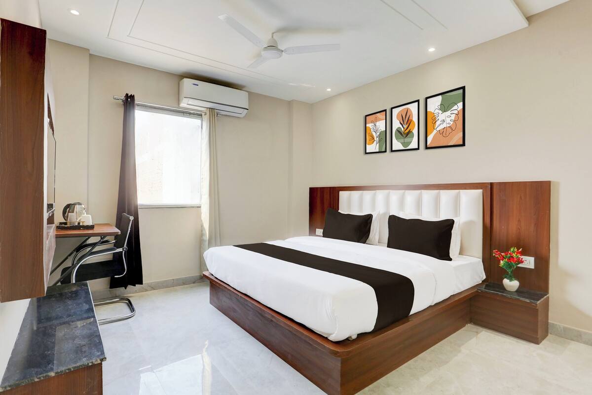 Habitación de hotel con cama, escritorio, silla, equipo de aire acondicionado y obra de arte en la pared.