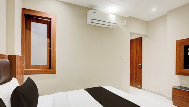 A hotel room with a bed, a wooden wardrobe, a mirror, and an air conditioning unit. - Super Townhouse Taj Nagri Phase 2 (Agra)