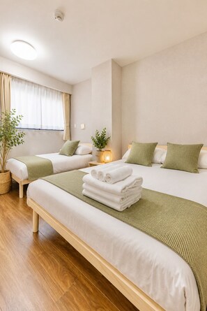 Ein Hotelzimmer mit zwei Betten, einem Blumentopf, einem Nachttisch mit Lampe und einem Fenster mit Vorhängen.