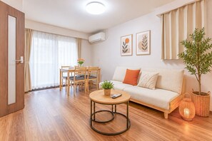 Ein modernes Wohnzimmer mit Sofa, einem Esstisch mit Stühlen, einem kleinen runden Tisch mit Fernbedienung, einer Zimmerpflanze und einer Wand-Klimaanlage.