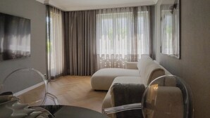 Una habitación de hotel moderna con un ventanal grande, un sofá, un televisor y una zona de comedor.