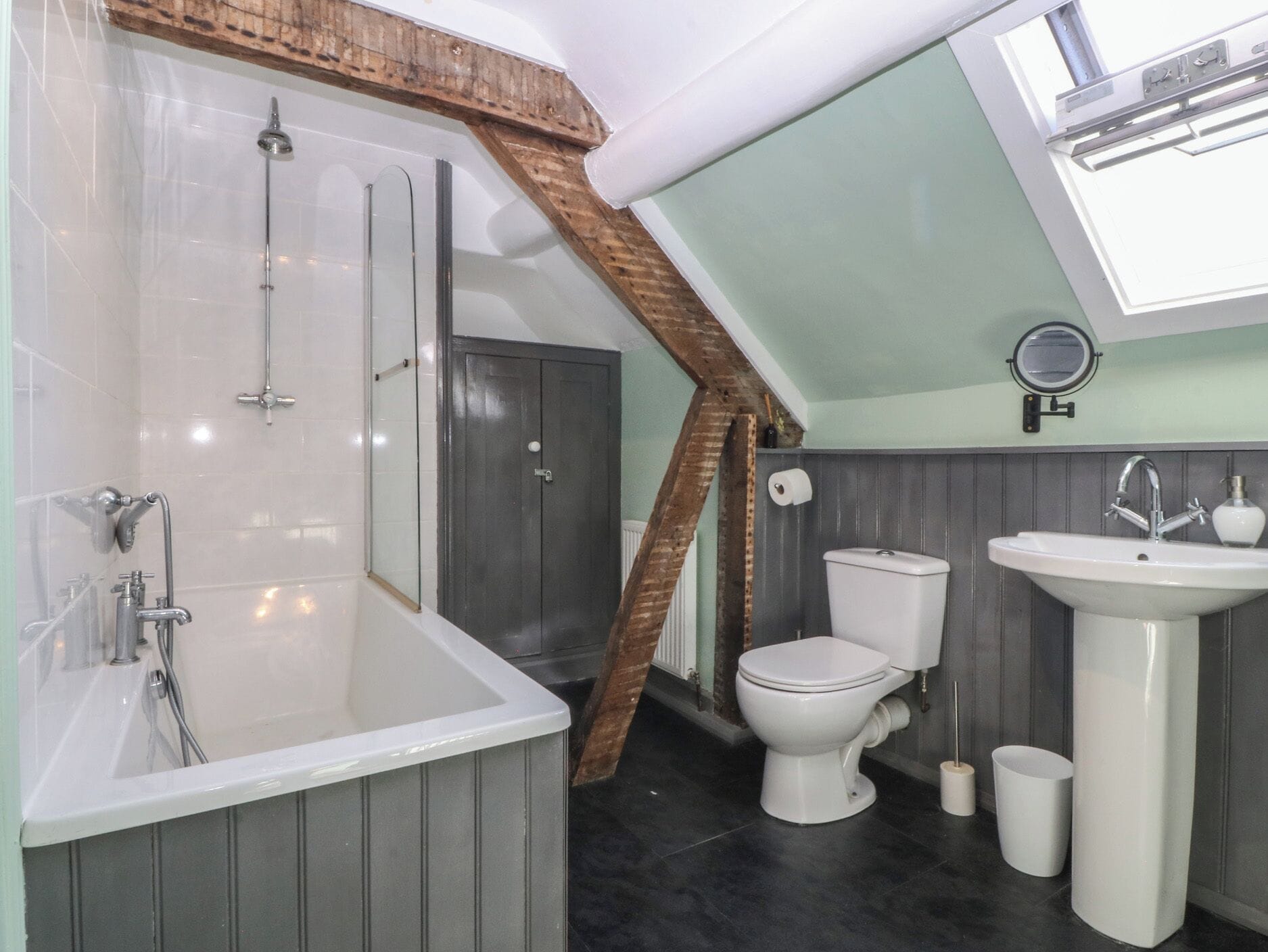 Un baño con bañera, inodoro y lavamanos, que presenta un techo inclinado y vigas de madera.