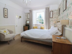 A bedroom with a bed, a dresser, a chair, a window with curtains, and a chandelier. - Tan y Gader (Dolgellau)