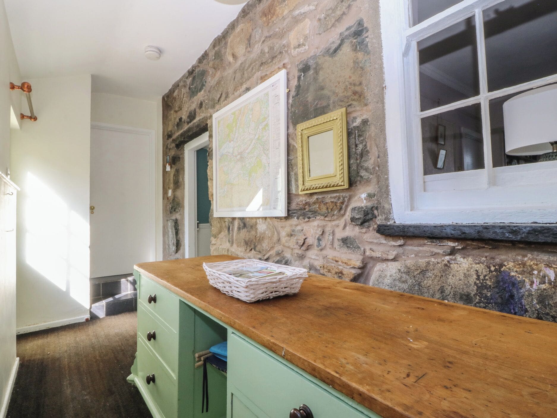 A room with a stone wall, a wooden counter, a green cabinet, and a window with a white frame.