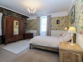 A bedroom with a bed, a dresser, a mirror, a radiator, and floral wallpaper.