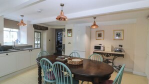 Un comedor con una mesa de madera, cuatro sillas, una cocina con armarios blancos, un microondas y un tostador.