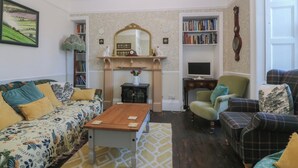 Una sala de estar con sofá, sillón, una mesa de centro de madera, chimenea, estantería y televisor.