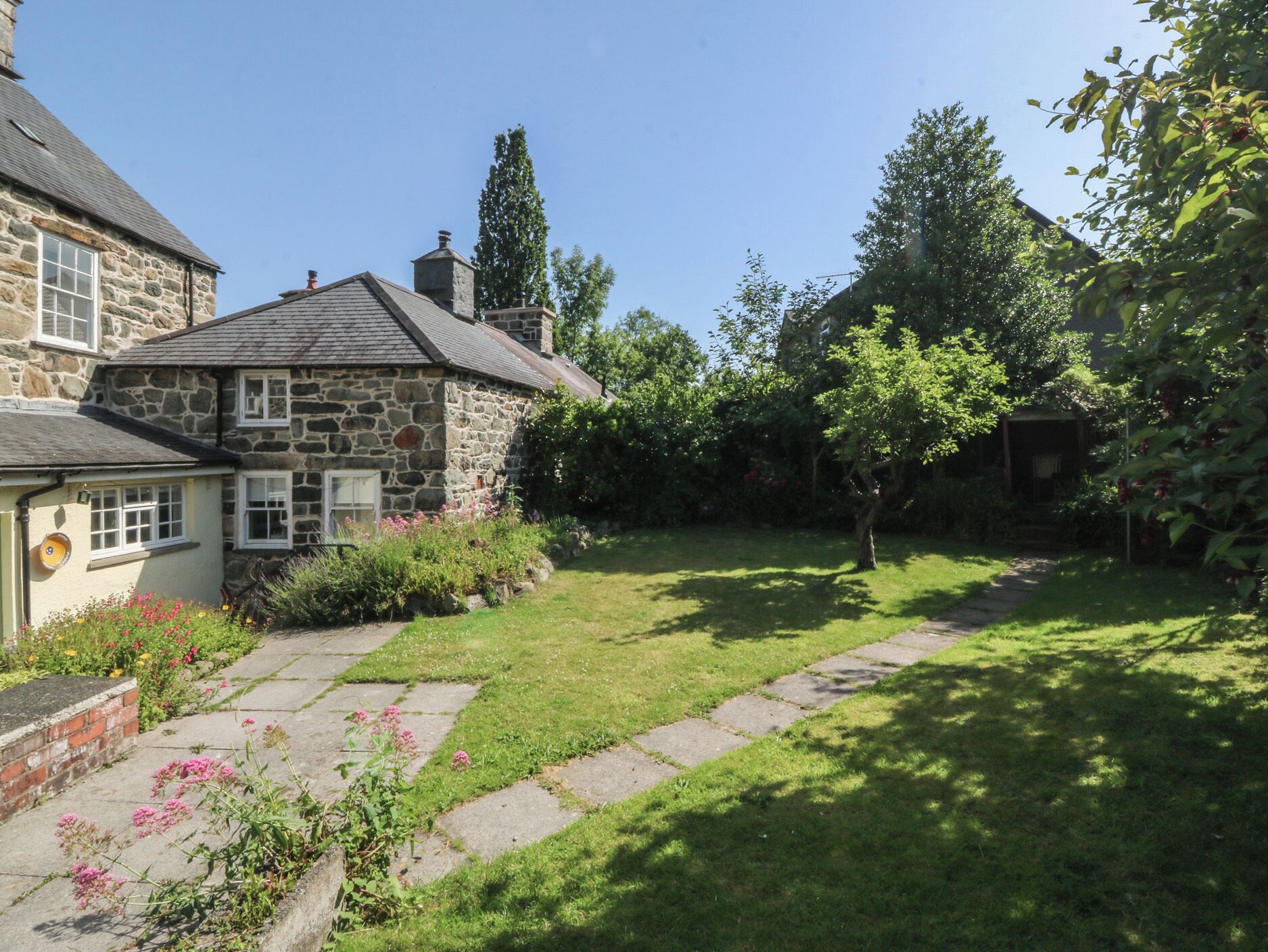 A stone house with a garden, a stone pathway, and a lawn.
