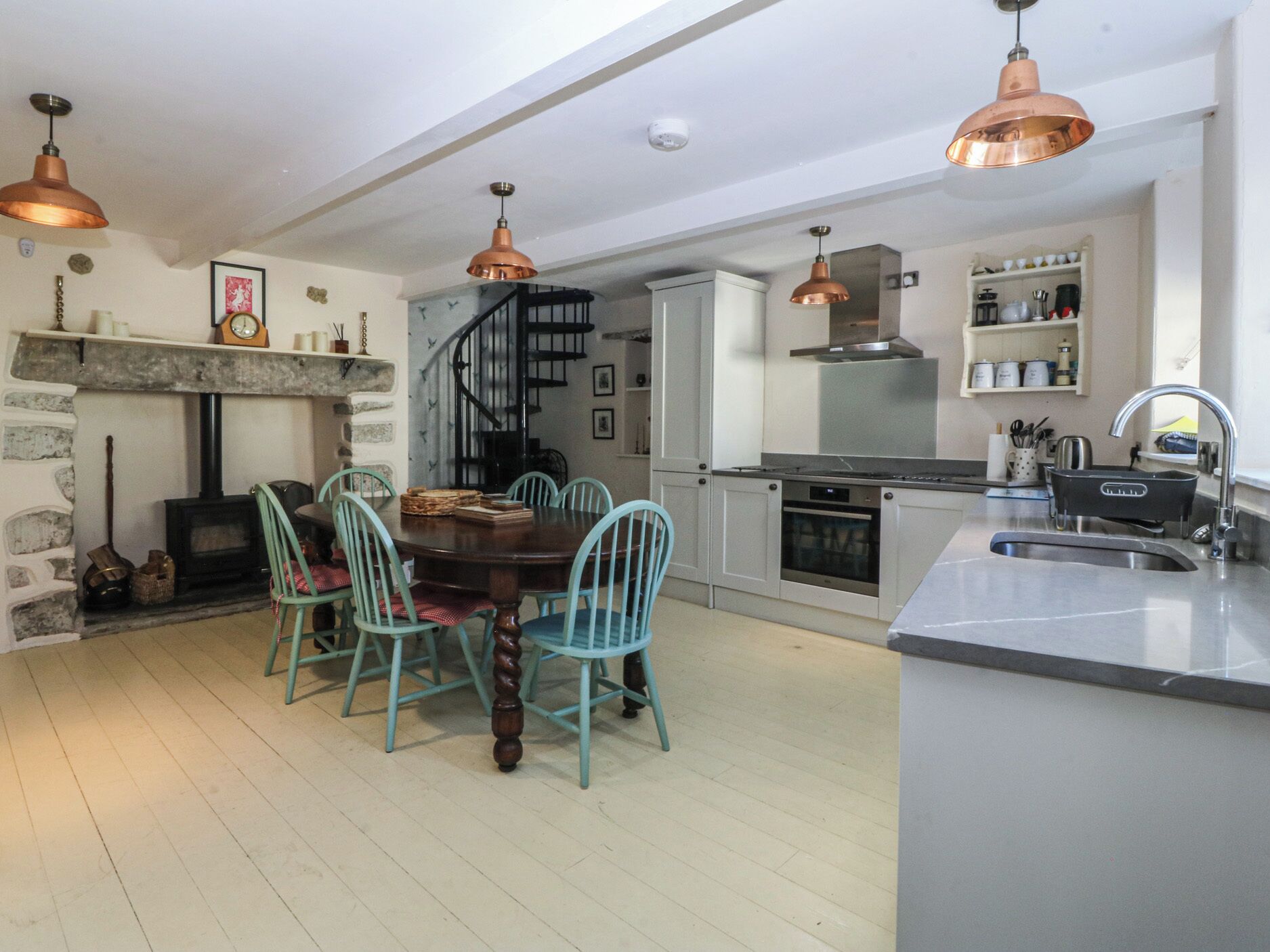Una cocina moderna con una isla central, una zona de comedor con sillas, una chimenea y una escalera.