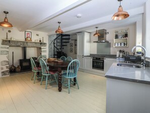 Una cocina moderna con una isla central, una zona de comedor con sillas, una chimenea y una escalera.