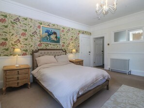 Un dormitorio con una cama, dos mesitas de noche, un radiador, una puerta y una ventana.