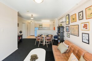 Ein modernes Wohnzimmer mit Sofa, Esstisch und Stühlen, Küchenzeile mit Schränken und gerahmten Bildern an der Wand.