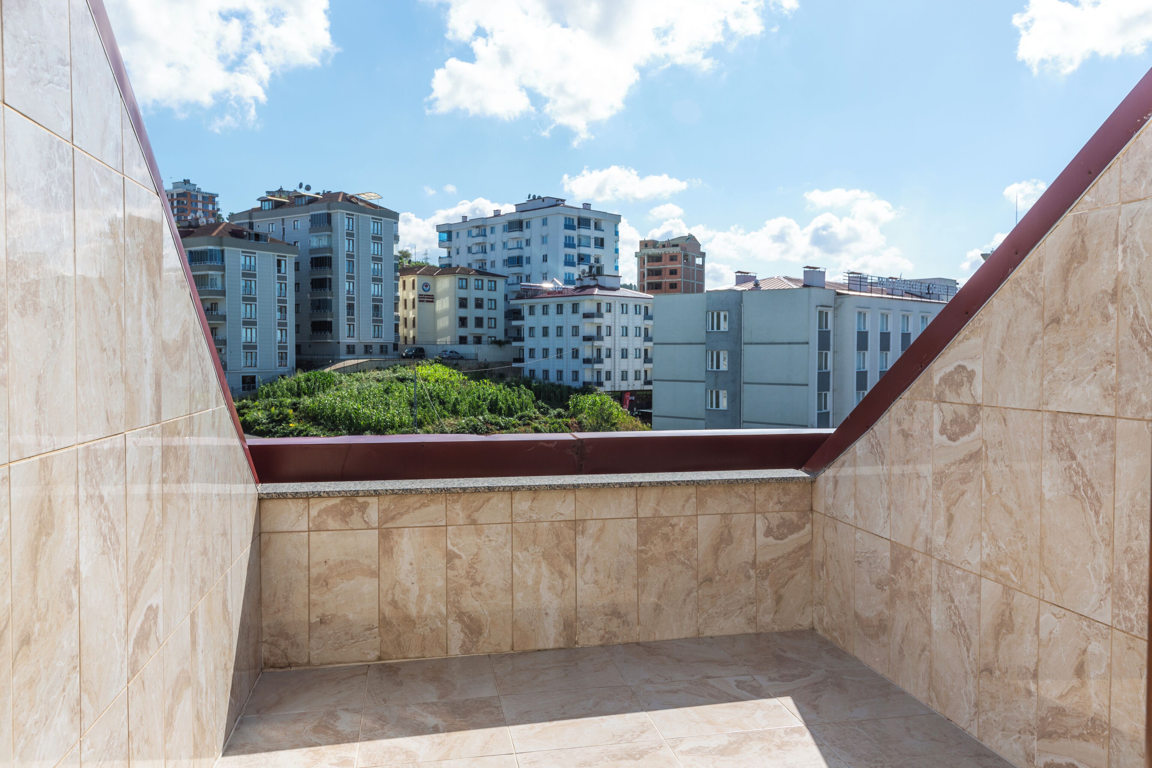 A view from a balcony with a tiled floor and a red railing, overlooking a row of multi-story residential buildings.