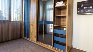 A room with a large wardrobe, a television mounted on the wall, and a window with sheer curtains.