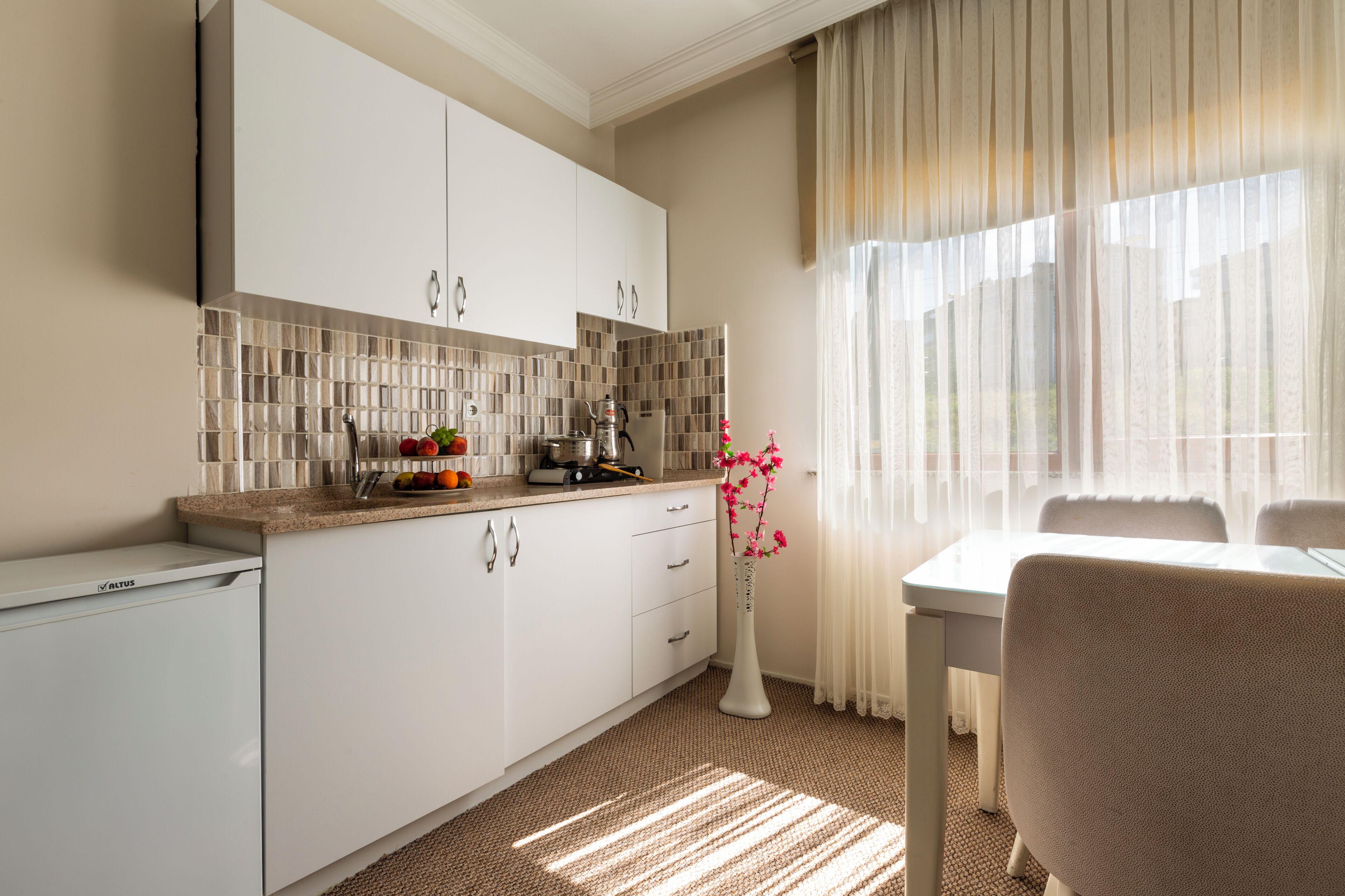 Una cocina moderna con armarios blancos, un salpicadero de azulejos y un comedor con mesa y sillas.