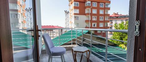 A balcony with a chair and table, a metal railing, and a view of multi-story buildings.