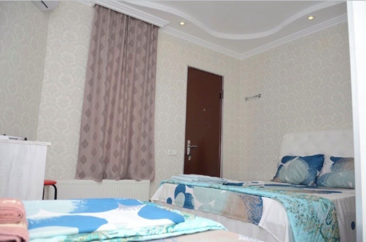 A hotel room with two beds, a door, a radiator, and a window with curtains.
