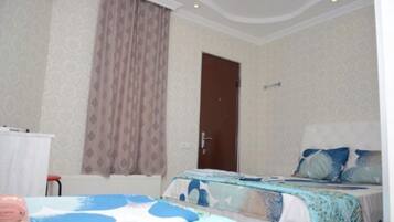A hotel room with two beds, a door, a radiator, and a window with curtains.