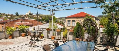 Une terrasse sur le toit, avec une table et des chaises, des plantes en pot et une vue sur les bâtiments en arrière-plan.