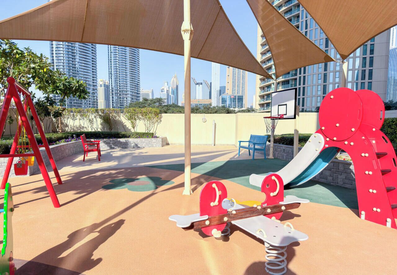 An outdoor play area with swings, a slide, and a basketball hoop.