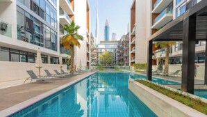 Un hôtel moderne doté d’une piscine centrale, de nombreux balcons et offrant une vue sur un gratte-ciel imposant en arrière-plan.