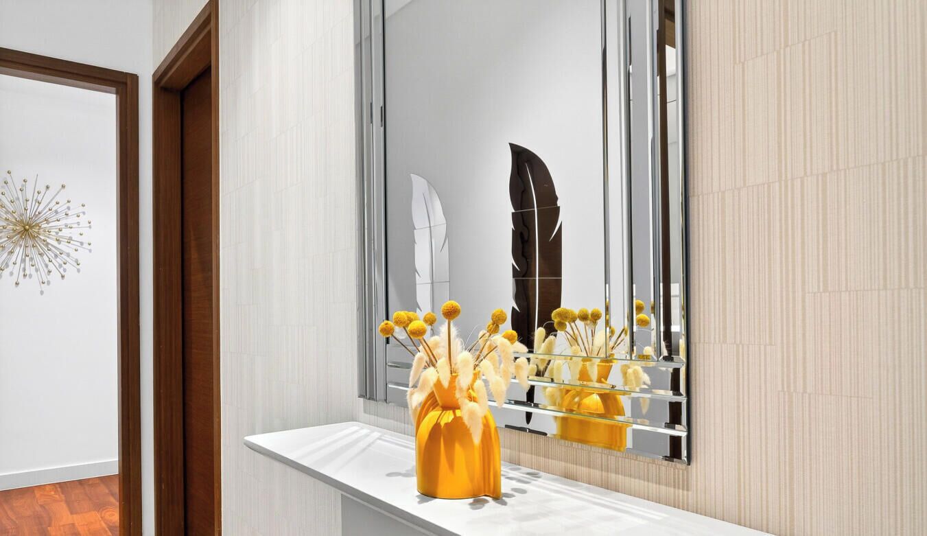 A bathroom with a mirror, a white vanity, and a yellow vase with dried flowers.