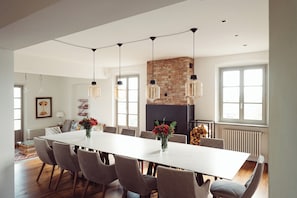 A spacious dining area with a long table, multiple chairs, hanging pendant lights, a brick fireplace, and large windows. - Scarpa Villas (Piemonte)