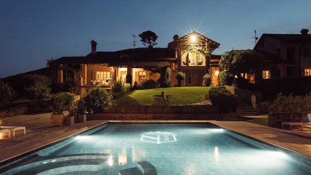 A swimming pool with a logo, a house with a light on the roof, and a well-maintained lawn. - Scarpa Villas (Piemonte)