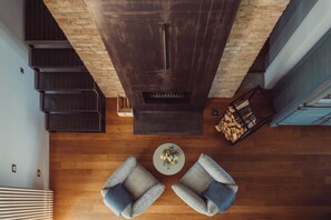 A top-down view of a room with a wooden floor, two patterned chairs, a round coffee table, a brick wall, and a staircase. - Scarpa Villas (Piemonte)