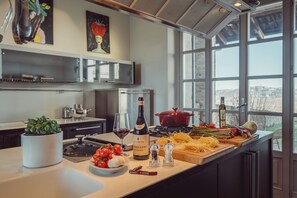 A modern kitchen with a large island, a red pot, fresh vegetables, and a wine bottle.